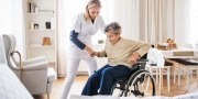 Een zorgmedewerkster helpt een oude dame op te staan vanuit haar rolstoel