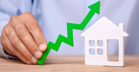 Stijgende huizenprijzen, man houdt een groene stijgende pijl in zijn hand naast een icoontje van een huis